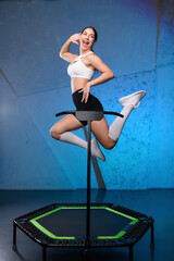 Energetic young fitness girl in white top and black shorts doing exercises jumping on mobile mini...