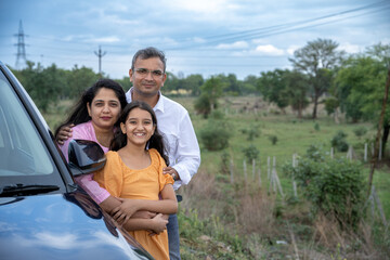 Indian couple showing nature or birds to little girl kid in front of car - concept of family...