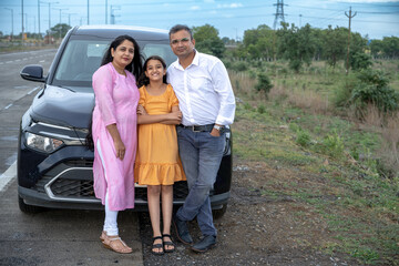 Indian couple showing nature or birds to little girl kid in front of car - concept of family...