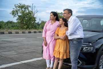 Indian couple showing nature or birds to little girl kid in front of car - concept of family...