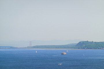 Obraz premium Wide blue river scene with distant hills, bridge and small passing boats on calm summer day