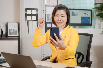 A middle-aged Asian woman sits at a work desk, deeply focused. Surrounded by charts and notes, she...