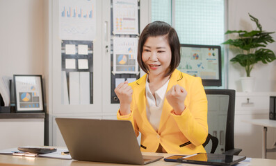 A middle-aged Asian woman sits at a work desk, deeply focused. Surrounded by charts and notes, she...