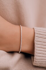 A close-up of a hand wearing a delicate bracelet, showcasing elegance against a soft, beige sweater.