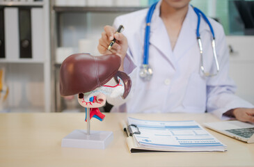A young Asian female doctor sits alone at her desk, carefully reviewing liver disease.She focuses...
