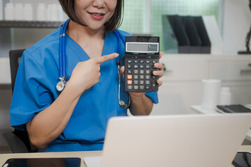 A middle-aged Asian female doctor sits alone at her desk in clinic, attentively reviewing patient...