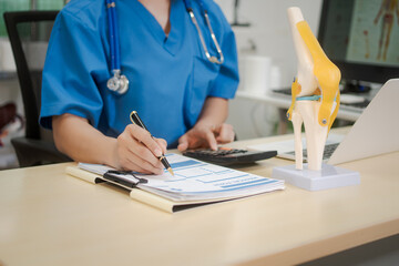 A middle-aged Asian female doctor at her desk,explaining various bone and joint diseases like arthritis,osteoporosis,and spinal disc degeneration,offering professional guidance in a clinical setting