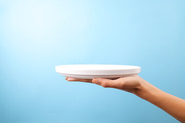 Hand Presenting Empty White Plate Against Blue Background