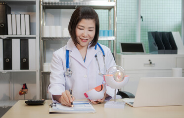 A middle-aged Asian female doctor holds an eye model at her desk, explaining eye anatomy and vision...