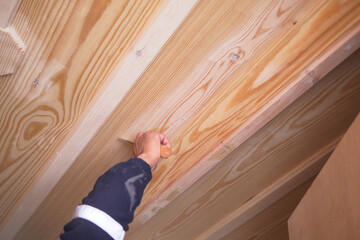 Hand applying finishing touches to wood ceiling in workshop