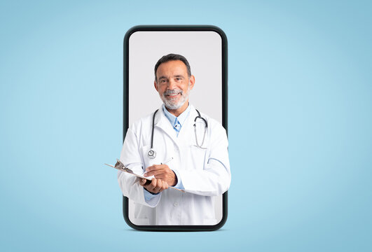 Happy confident european old doctor in white coat with stethoscope makes notes on big phone screen on blue background. App for medical help, diagnostics, exam, ad and offer
