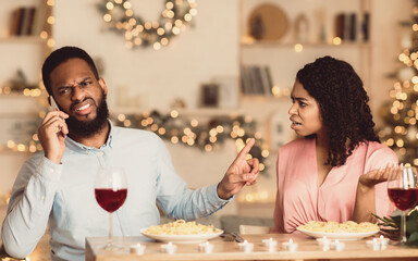 Annoyed african american woman looking at her man who talking on mobile phone and showing her...