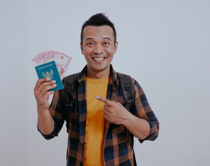 Happy asian man tourist traveler pointing his passport full of money, isolated on white background.