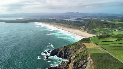 A stunning aerial view captures majestic cliffs, lush greenery, and a serene beach along the...