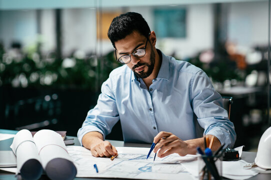 Concentrated busy handsome millennial islamic male engineer with beard in glasses, think about project in office interior, professional architect work in factory. Solving construction planning problem