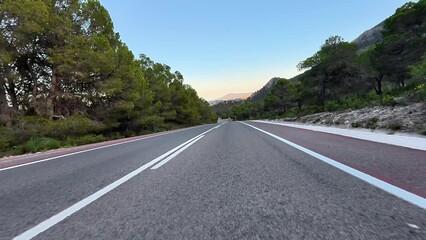 A beautiful and picturesque winding road encircled by lush greenery and majestic mountains as the sun sets