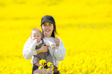A Japanese mother in her 30s holding her 6-month-old baby boy stands in a fully blooming field of...