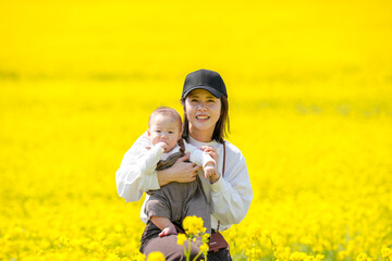 A Japanese mother in her 30s holding her 6-month-old baby boy stands in a fully blooming field of...