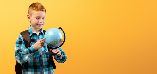 Positive schoolboy with backpack holding globe, studying geography on yellow studio background, copy space. Happy boy going to school, enjoying his school days. Kids education concept