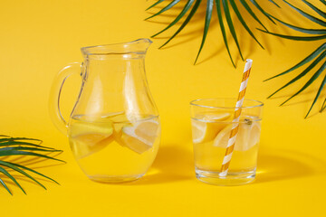 Homemade lemonade in a decanter and a glass with a paper straw on a yellow background