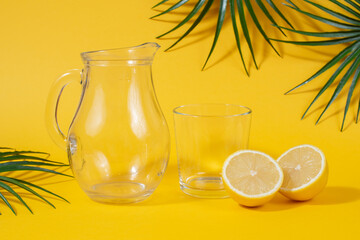 Transparent decanter and glass with cut lemon on yellow background