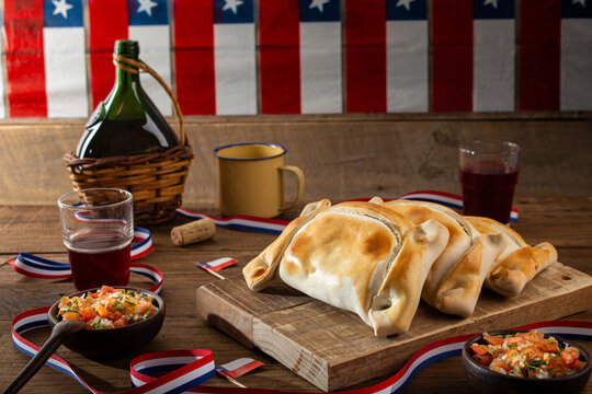 Chilean Independence Day concept. National holidays. Typical baked empanadas, with cup of wine Dishes and drinks for the September 18th celebration, wooden background, flag decoration