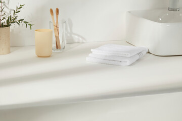 Bathroom sink with bamboo toothbrushes, soap bottle, folded towels, and green branches. Bright and fresh, reflecting a clean and conscious lifestyle.