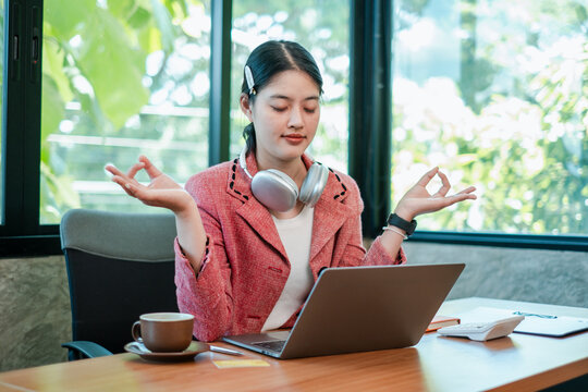 A young woman practices meditation at her desk, surrounded by modern office equipment, promoting work-life balance and mindfulness.