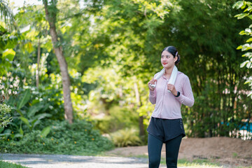 Woman in activewear with towel, enjoying a refreshing walk in a green park setting.