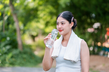 A young woman in a white tank top drinks water from a bottle while enjoying a refreshing moment in...