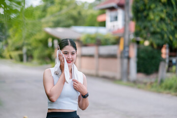 A young woman uses a towel to cool down after exercising outdoors in a suburban neighborhood...