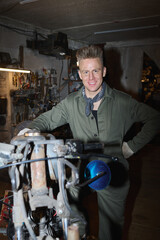 Portrait of young adult Caucasian man smiling while assembling and repairing custom bike in...