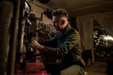 Caucasian young adult man repairing custom bike in workshop, sitting at workbench and using tools,...