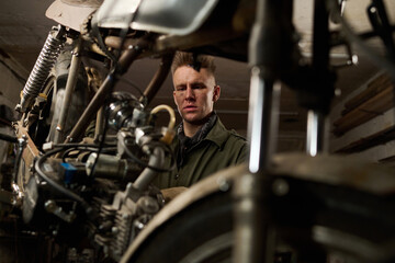 Caucasian middle aged man repairing custom motorcycle in workshop focusing on mechanical components...