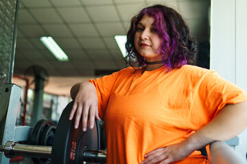 beautiful, overweight young latina posing happily and preparing to lift weights in a gym. positive, pushing herself to the limit. improvement and well-being.