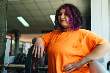 beautiful, overweight young latina posing happily and preparing to lift weights in a gym. positive, pushing herself to the limit. improvement and well-being.