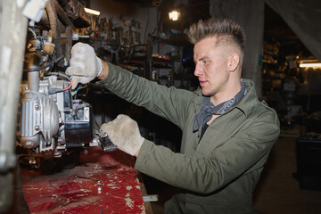 Caucasian young adult man repairing custom motorcycle in workshop, using tools and wearing...