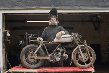 Middle aged Caucasian man wearing protective mask and gloves repairing custom motorcycle in...