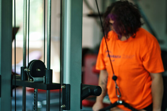 Beautiful overweight Latina woman wearing a uniform and colorful 80s-style makeup, exercising in a gym, doing push-ups on machines. Effort, improvement, and overcoming.
