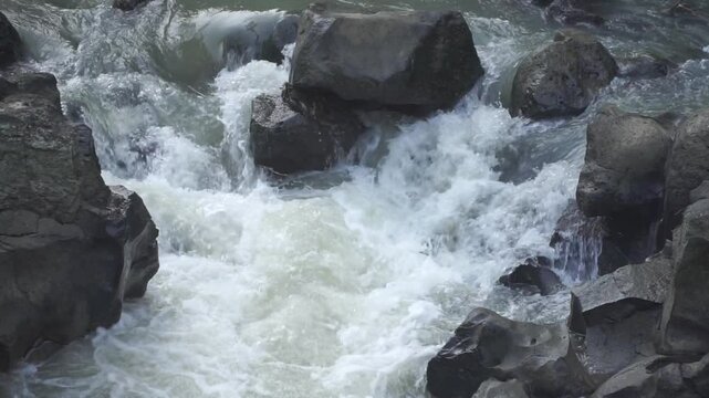 Close-up view of a powerful river current crashing against large rocks, creating intense white water and natural turbulence. Ideal for themes related to raw nature, force of water, and environmental.