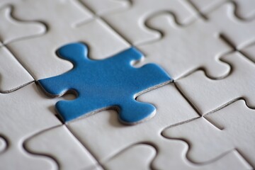 Fototapeta premium Minimalistic image of blue puzzle piece about to complete a white jigsaw puzzle