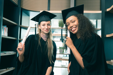 Happy Diverse Graduates Celebrating with Diplomas, Two Young Women in Graduation Caps and Gowns...