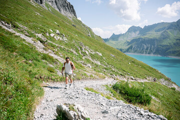 Hiker walking on mountain trail with trekking poles near lake