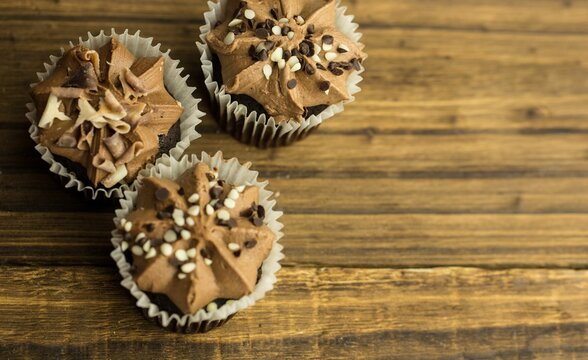 Naklejki Flat design is showing three chocolate cupcakes with swirled frosting and sprinkles on wooden table