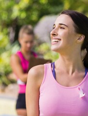 Close-up of smiling caucasian young woman with pink awareness ribbon on chest exercising in park