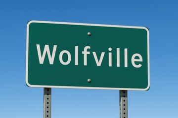 Green road sign displaying "Wolfville" under a clear blue sky, indicating town entrance, travel direction, or Nova Scotia location.