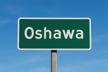 Green road sign showing "Oshawa" against a bright blue sky, representing city entrance, travel direction, or Ontario destination.