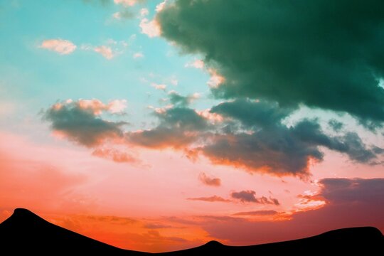 Fototapeta Silhouetting sand dunes in flat design merging sunset orange into teal sky with glowing clouds