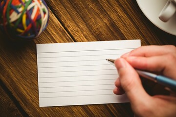 Cropped hand writing in book with cup on table