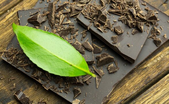 Naklejki Broken dark chocolate bar is being shown on wooden table in flat design with green leaf